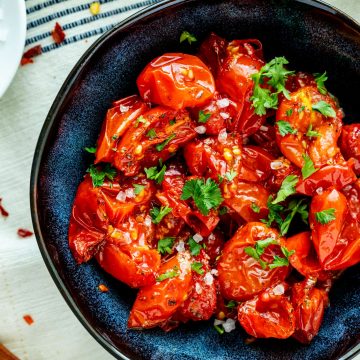 Square close up overhead photo of air fryer tomatoes in a blue bowl garnished with parsley.a