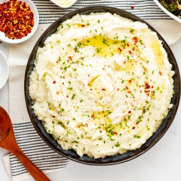 Overhead square photo of Boursin mashed potatoes in a blue bowl garnished with parsley and crushed red pepper flakes.
