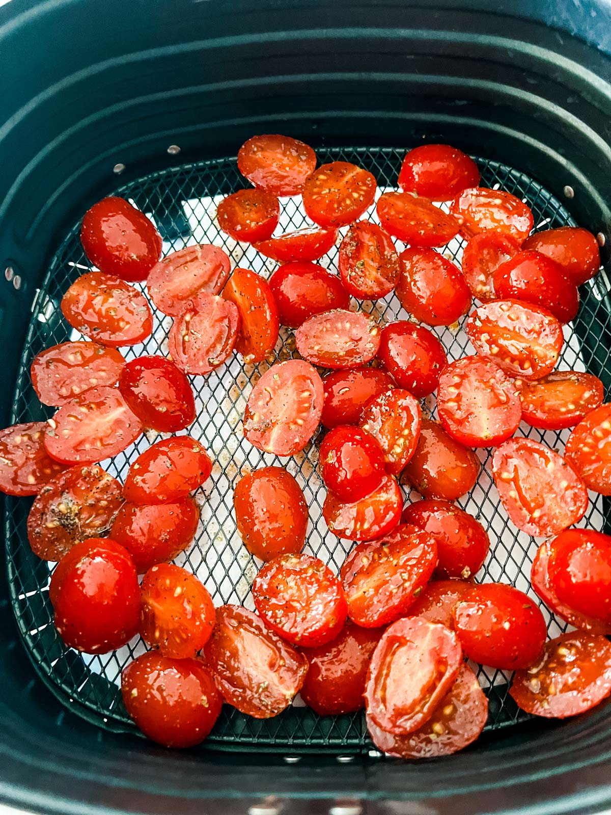 Halved grape tomatoes in an air fryer basket ready to cook.