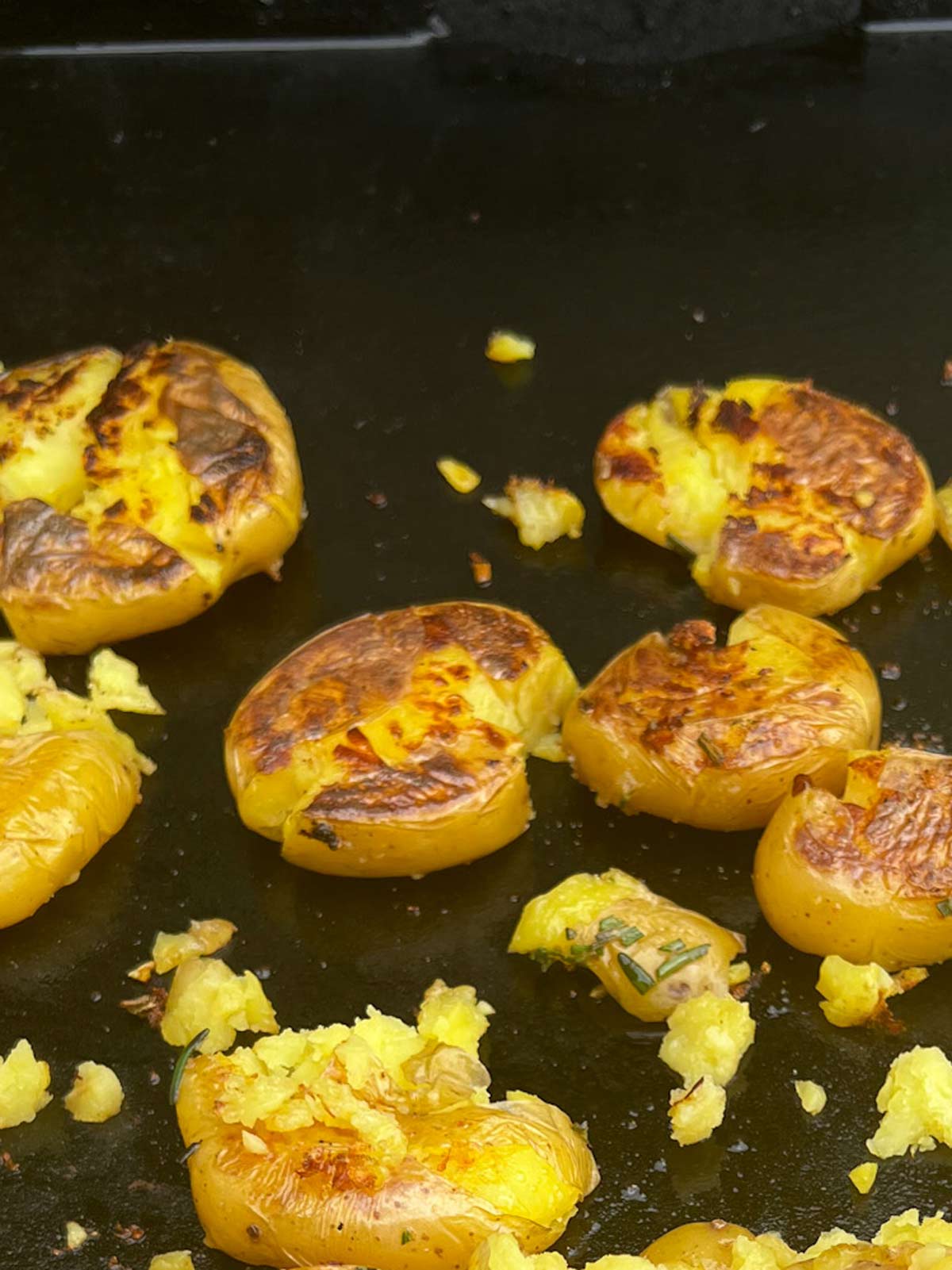 Smashed potatoes that have just been flipped on a Blackstone griddle.