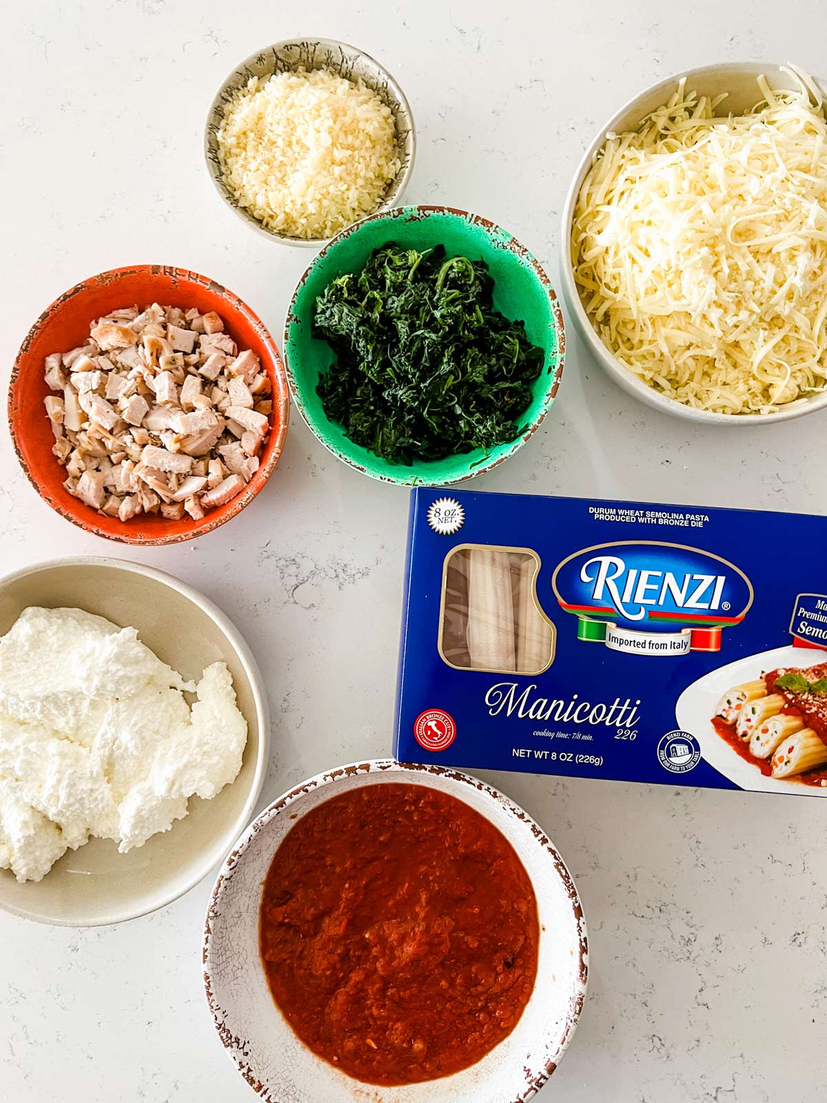 Overhead photo of manicotti, ricotta, chicken, spinach, mozzarella, parmesan, salt, pepper, and marinara sauce.