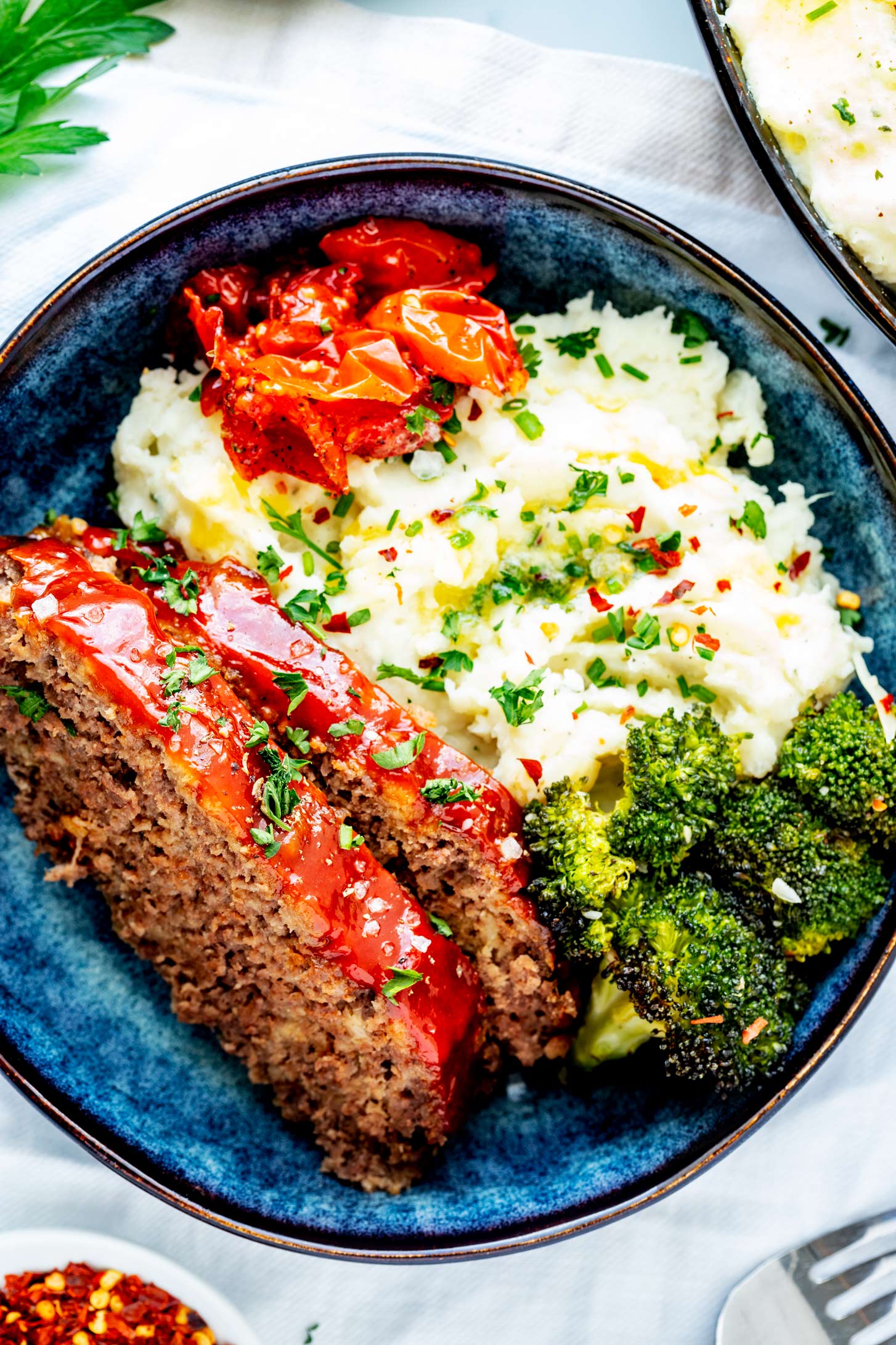 Overhead photo of crockpot meatloaf plated over a bed of mashed potatoes with roasted tomatoes and broccoli.