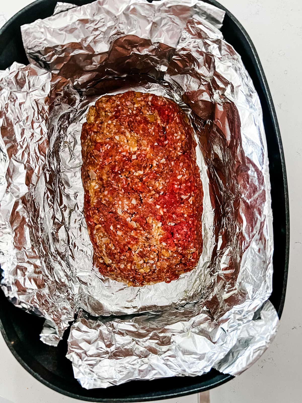 A meatloaf mixture in a slow cooker that has been lined with a foil sling.