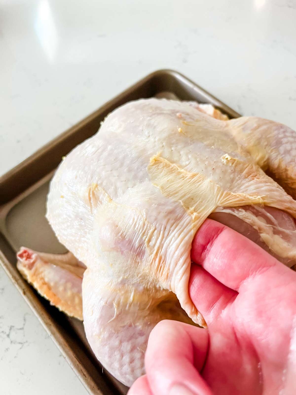Lifting up the skin from a whole chicken.