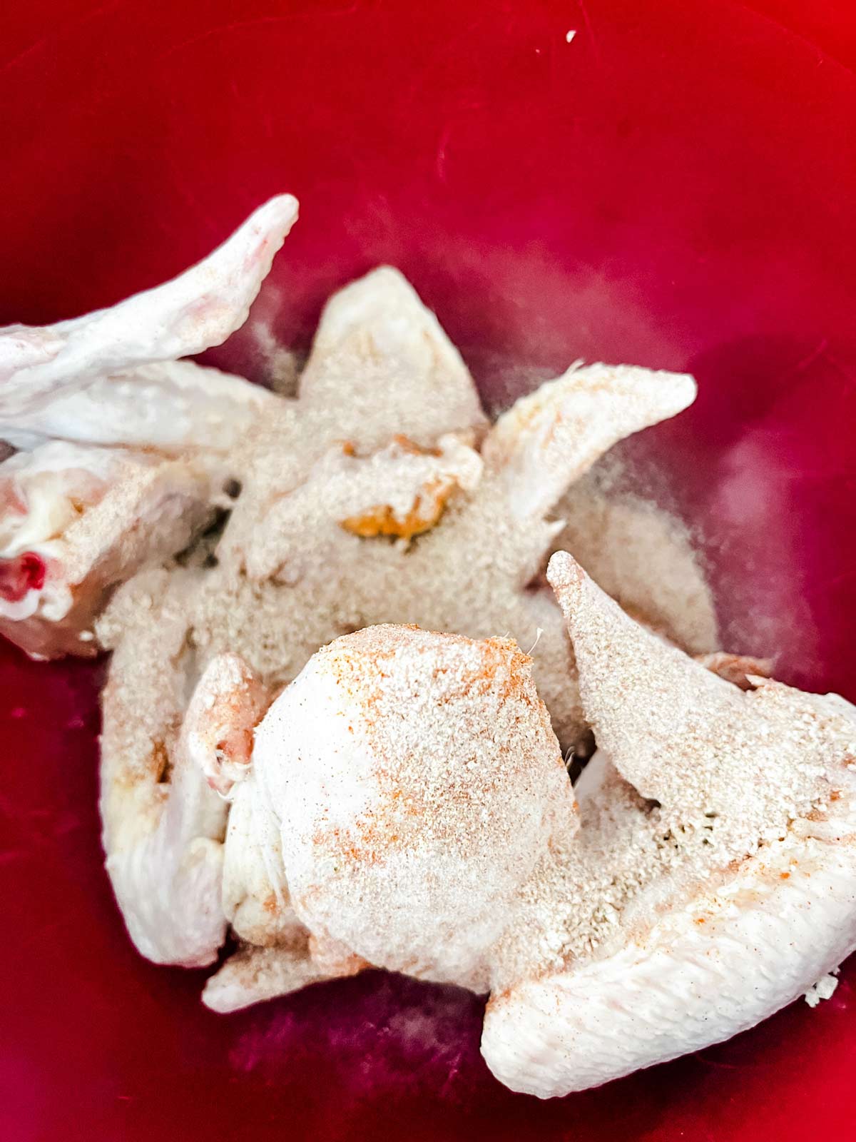 Seasonings poured over chicken wings in a red bowl.