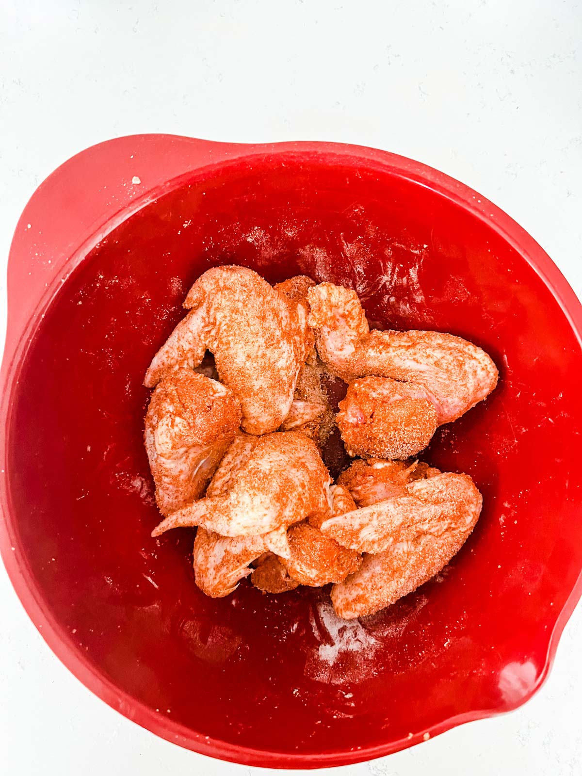 Chicken wings that have been tossed with seasonings in a red bowl.