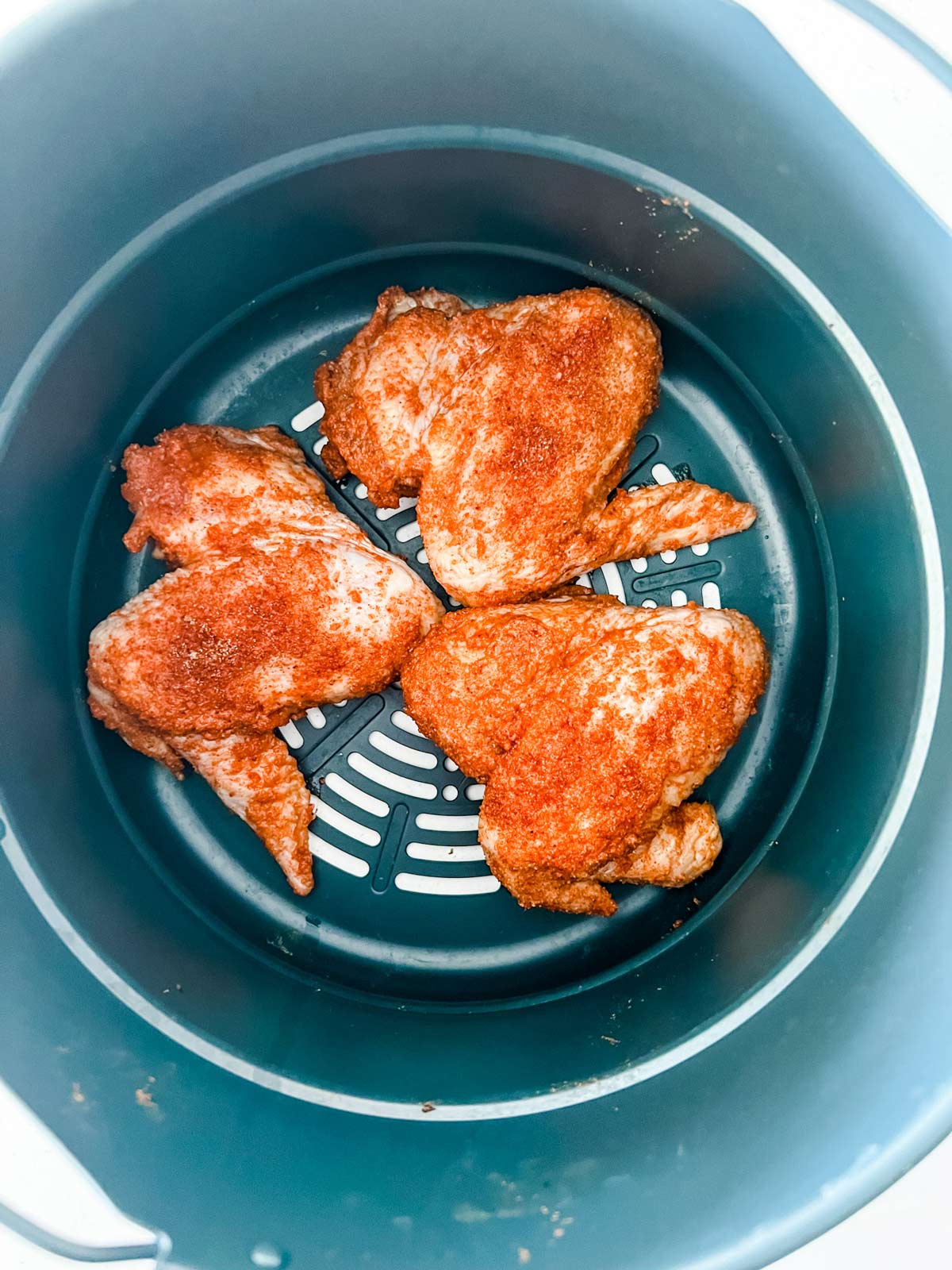 Seasoninged chicken wings in the air fryer basket of a Ninja Foodi.
