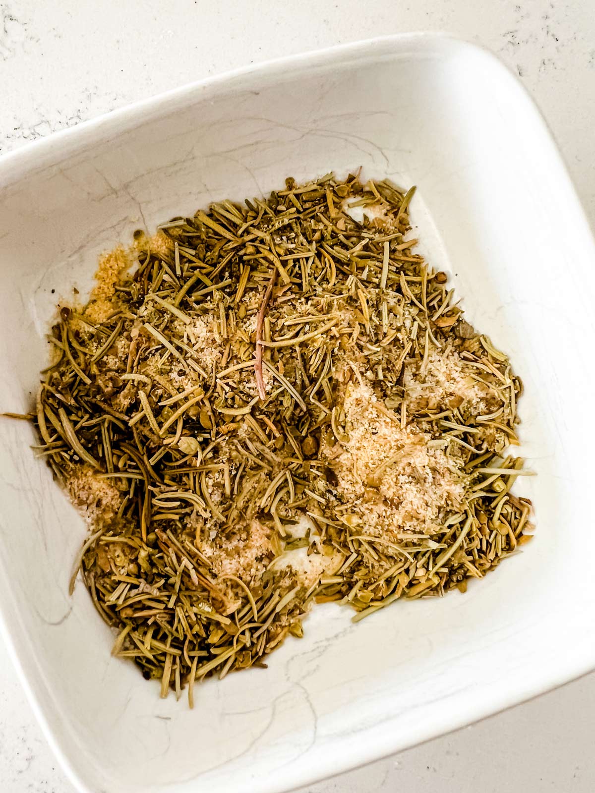 Photo of rosemary, oregano, salt, dried mustard, and garlic powder in a small bowl. 