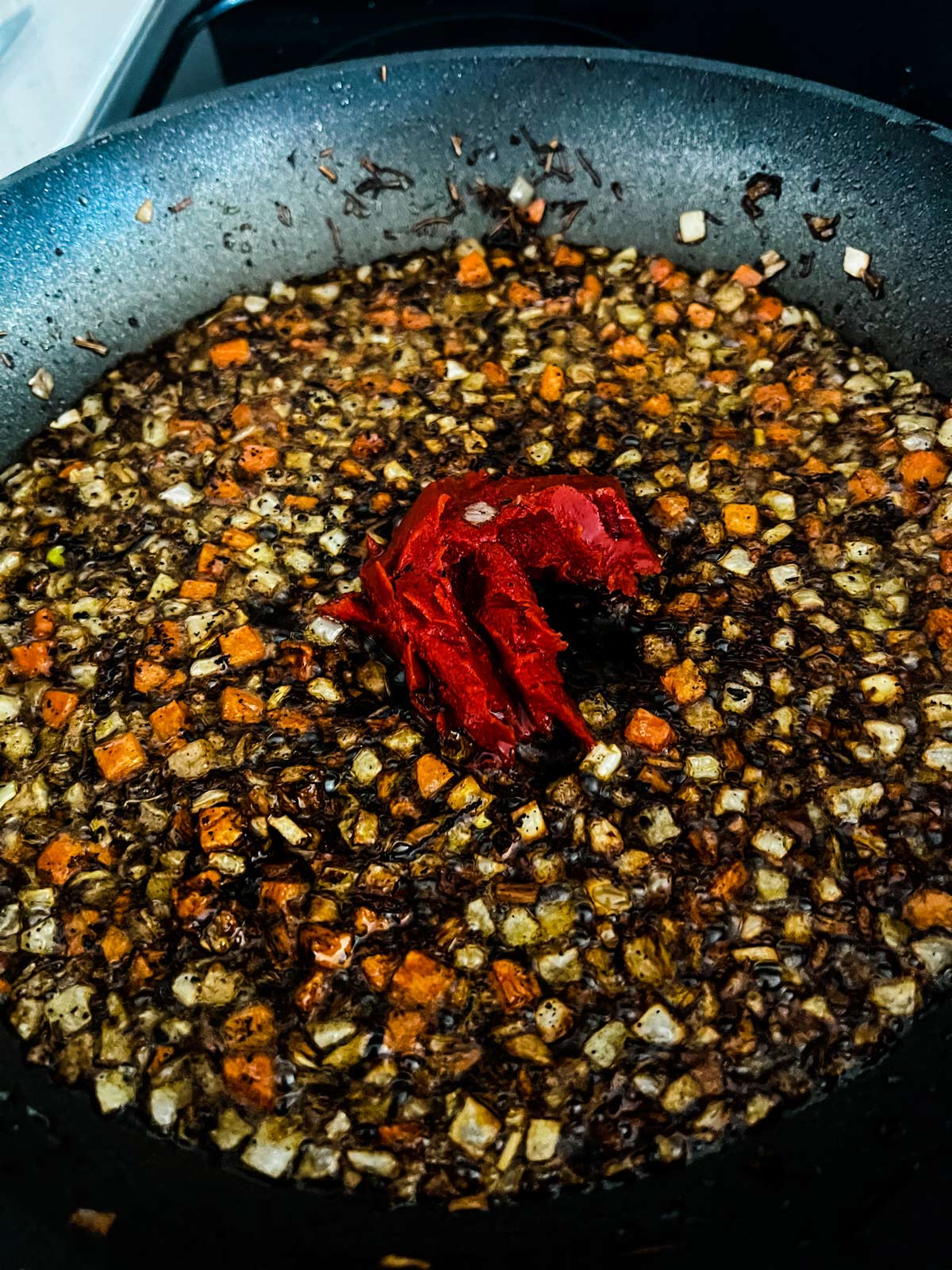 Tomato paste added to a skillet of sautéed vegetables.