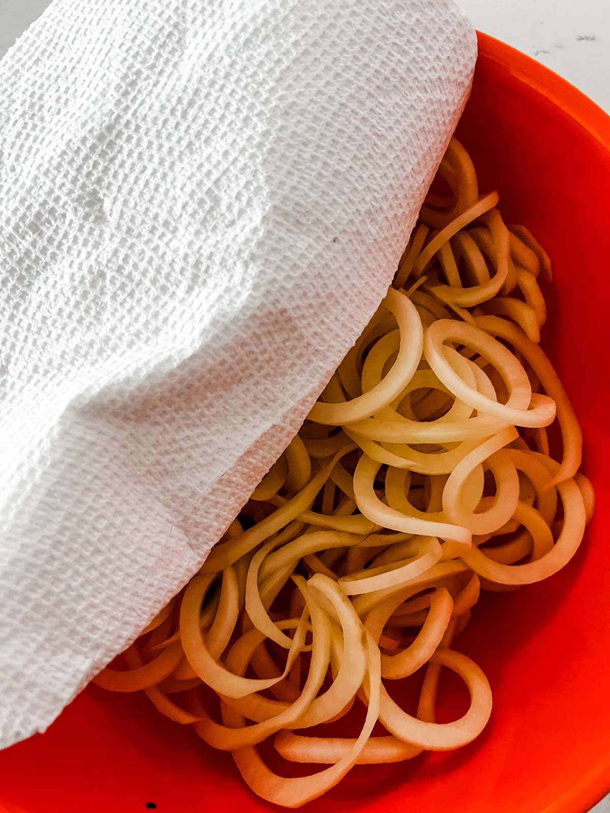 Spiralized potatoes that have been soaked being blotted dry with paper towels.