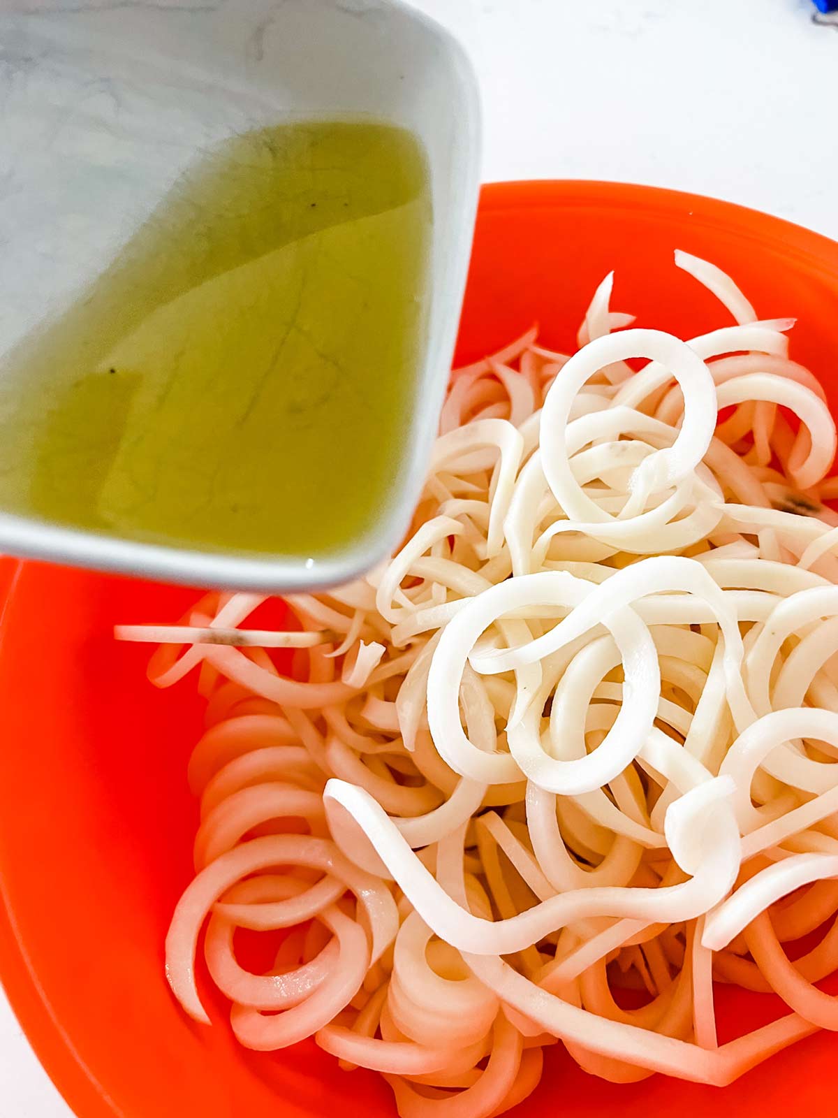 Spiralized potatoes in an orange bowl being tossed with oil.