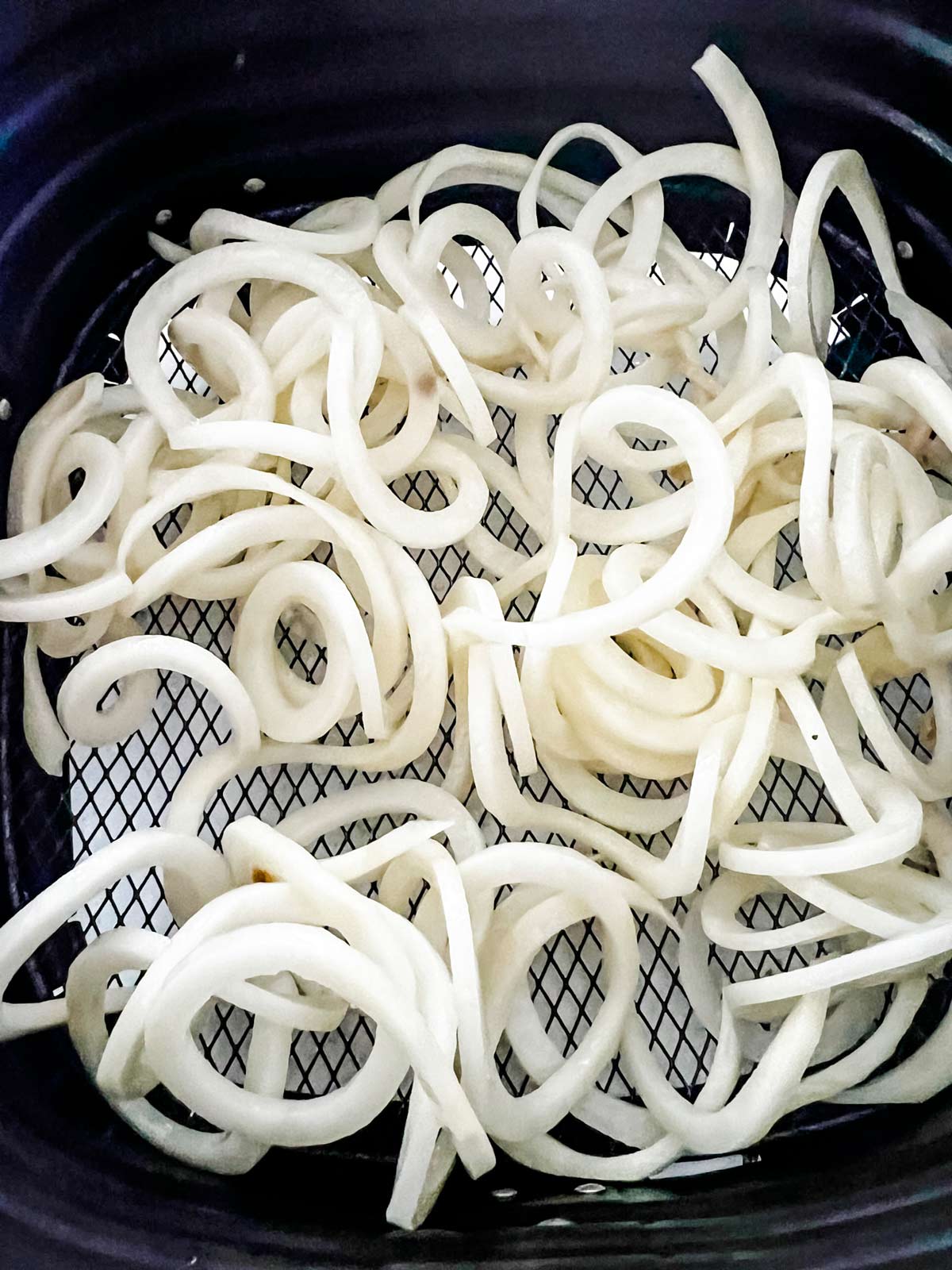 Curly fries in an air fryer basket ready to cook.