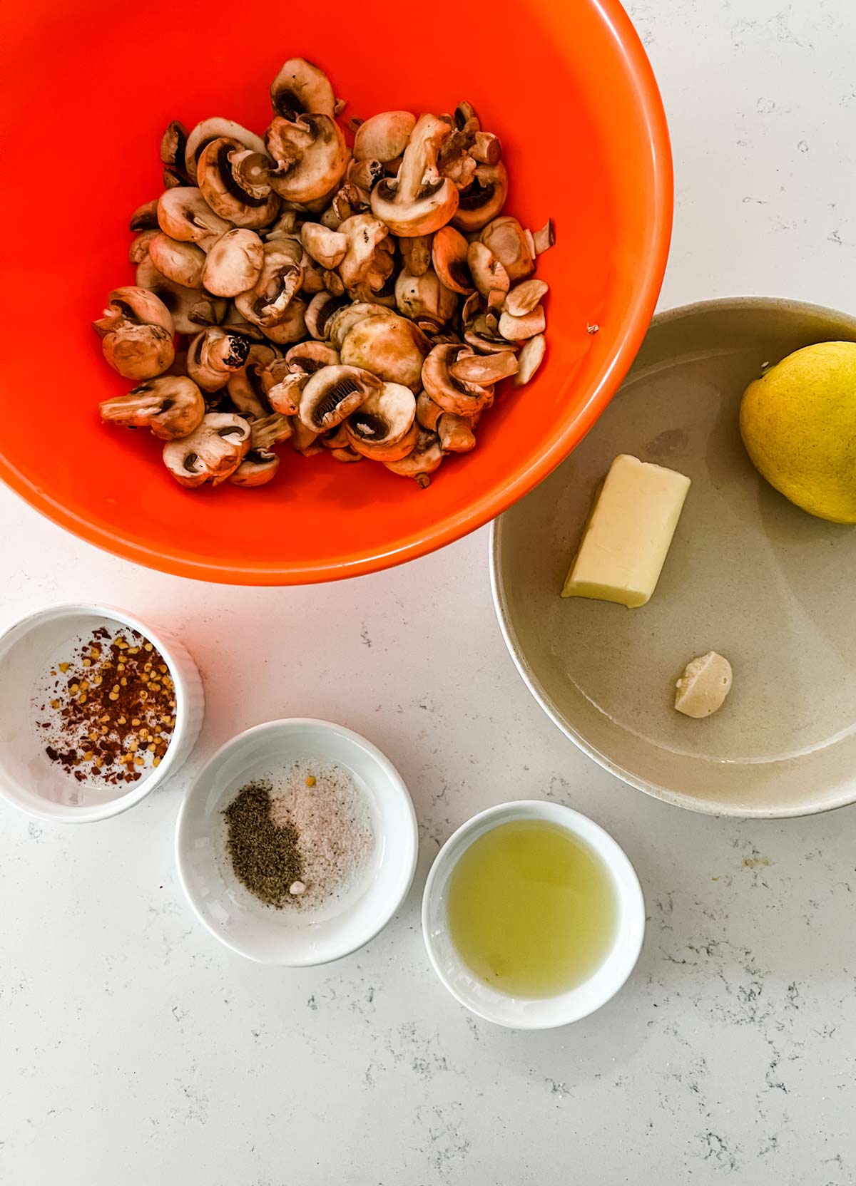 Photo of a bowl of mushrooms, lemon, butter, garlic, oil, and seasonings.