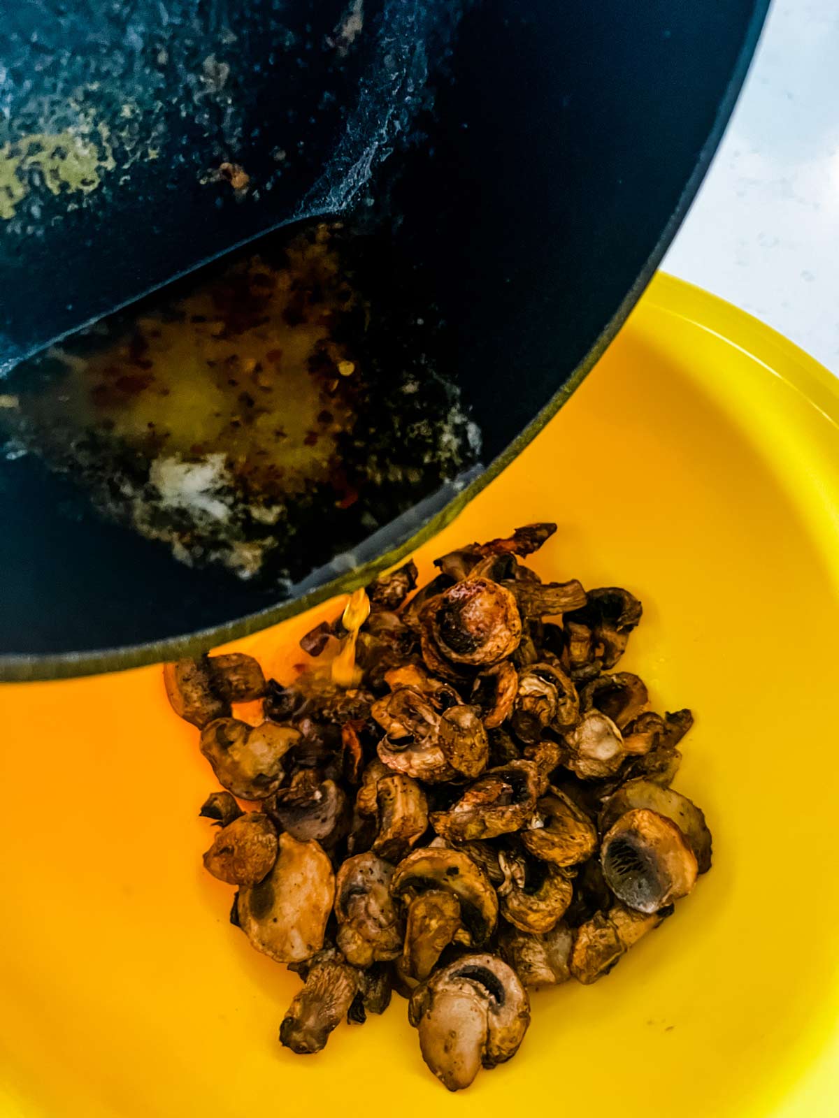 Butter being poured over air fryer mushrooms in a yellow bowl.