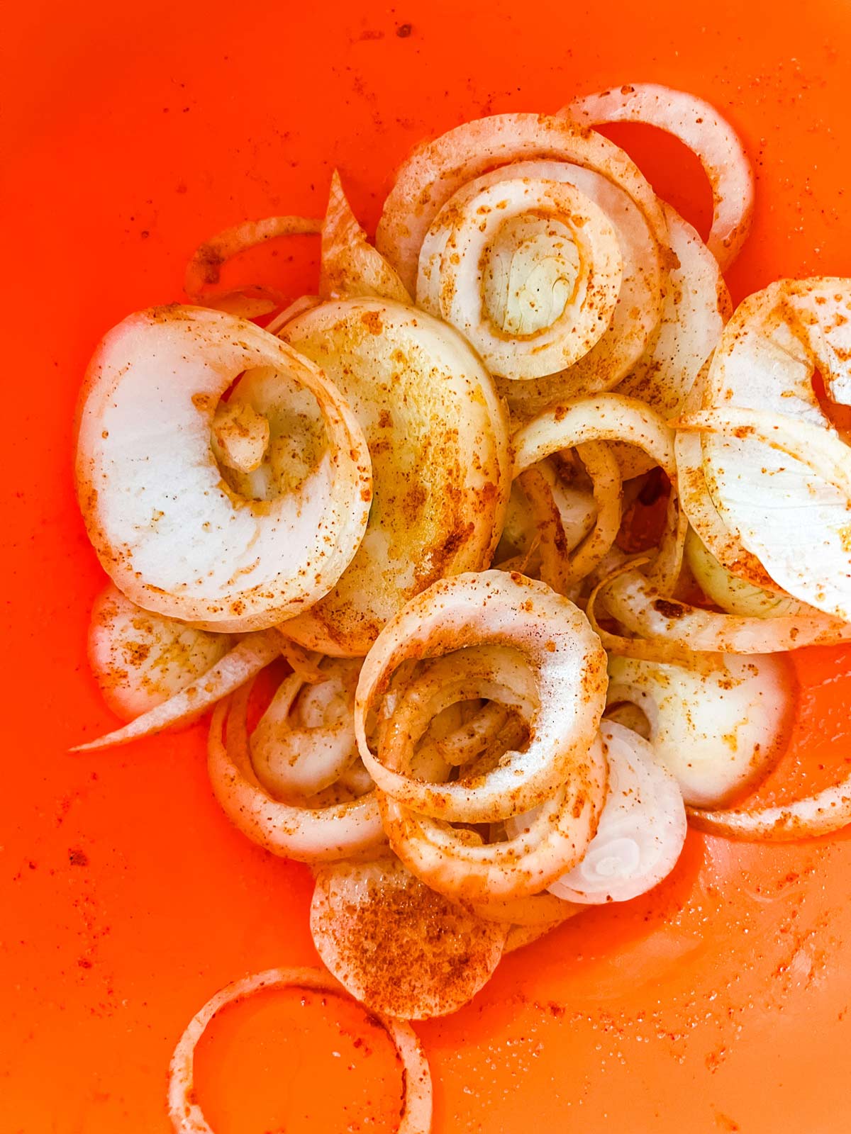 Seasonings tossed with sliced onions in an orange bowl.