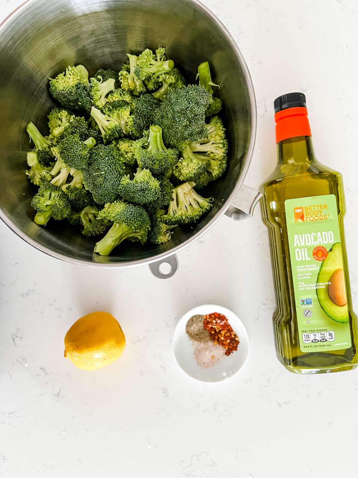 Overhead photo of a bowl of broccoli, avocado oil, lemon and seasonings.