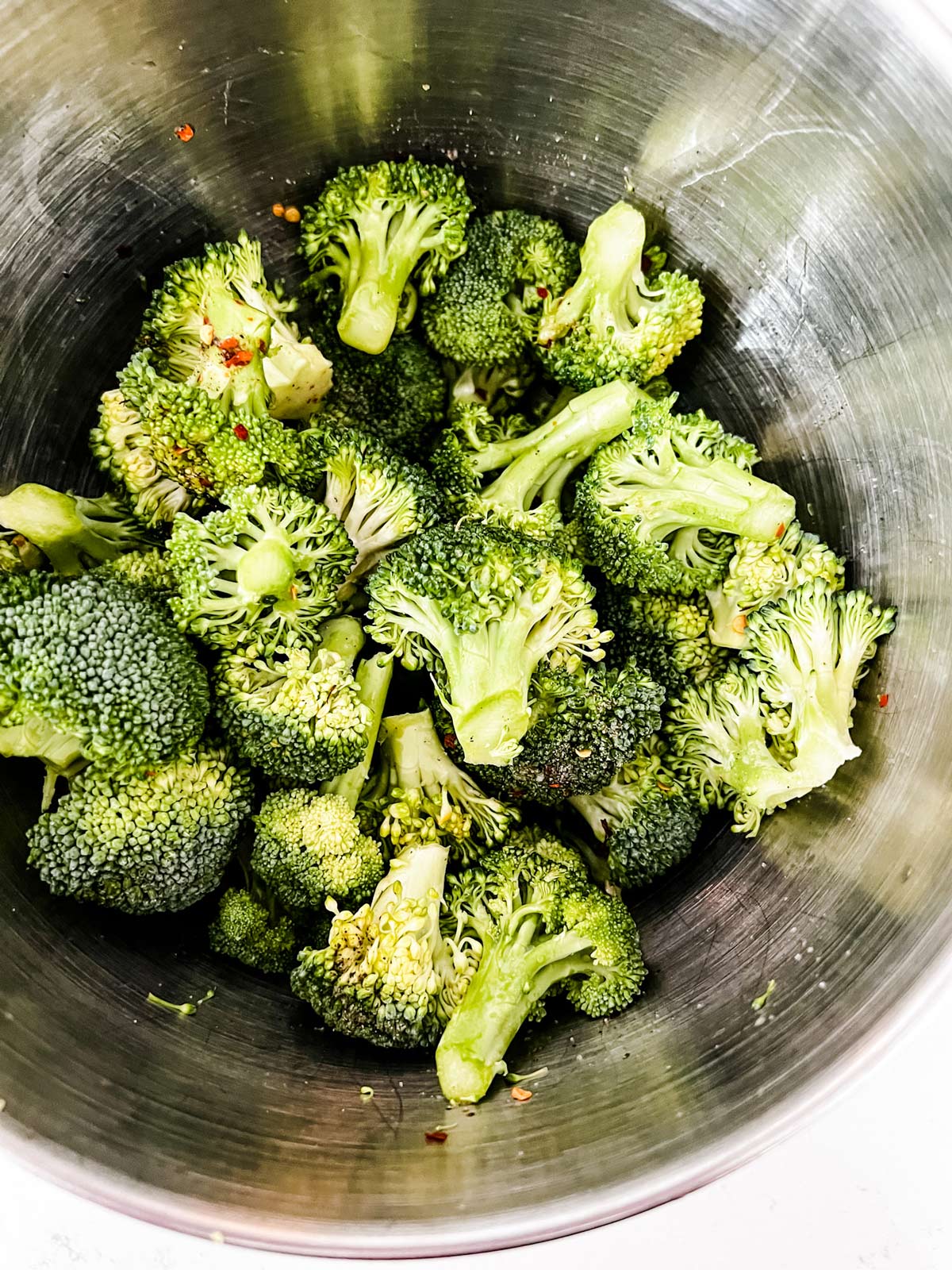 Broccoli florets tossed with seasonings in a bowl.