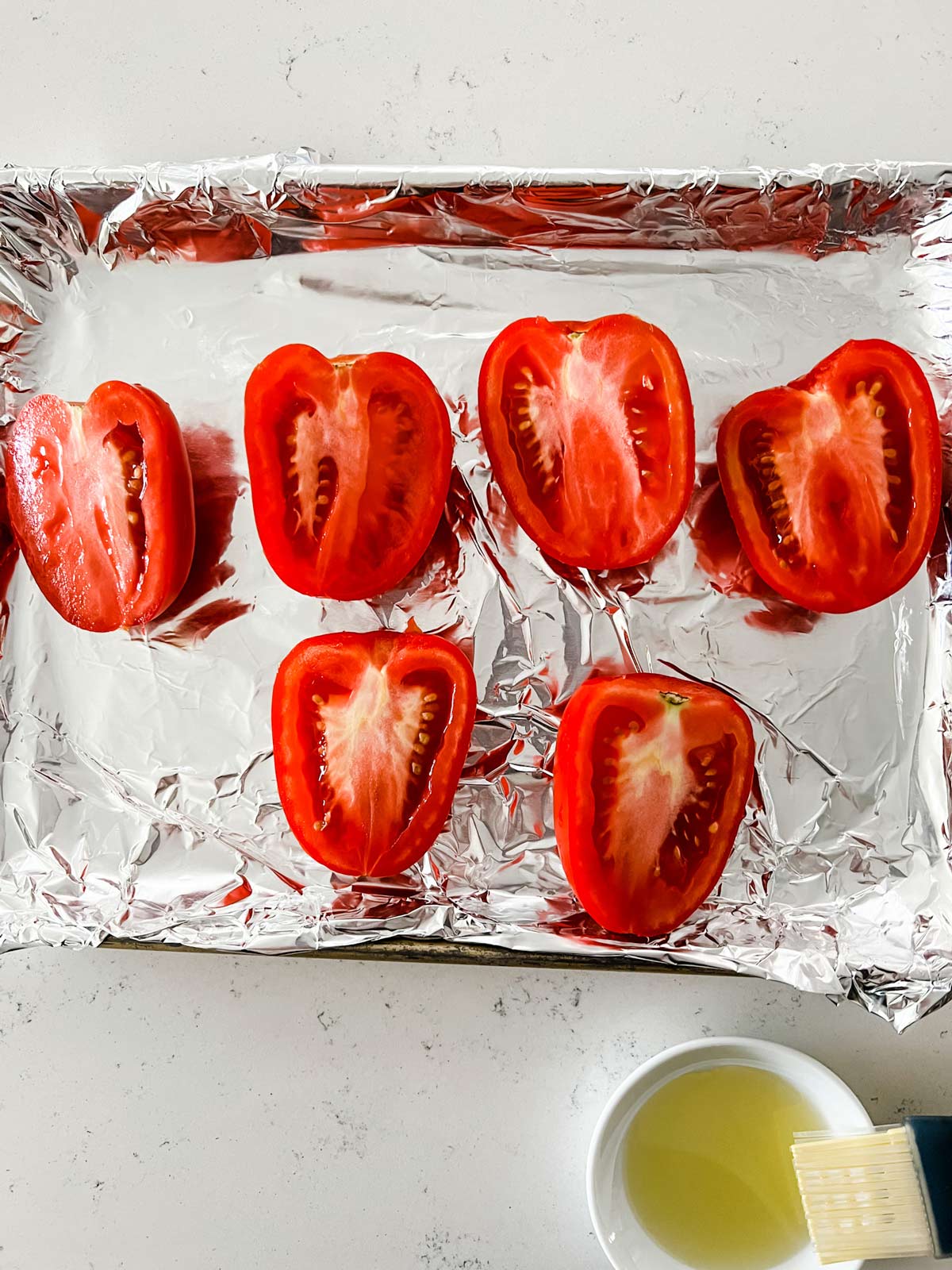 A foil lined sheet pan with halved tomatoes brushed with oil.