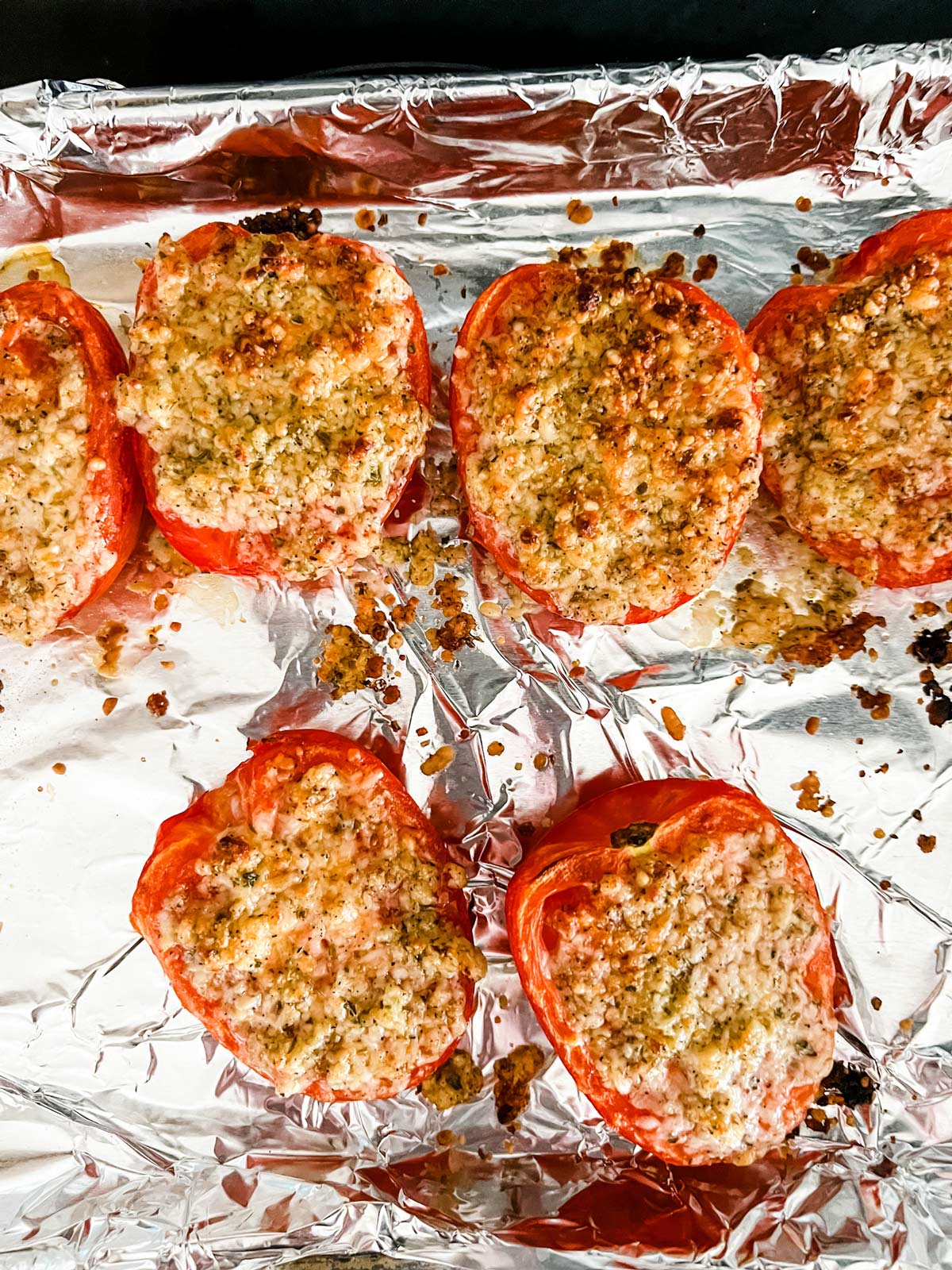 Parmesan, garlic and seasonings on top of broiled tomatoes on a foil lined sheet pan.