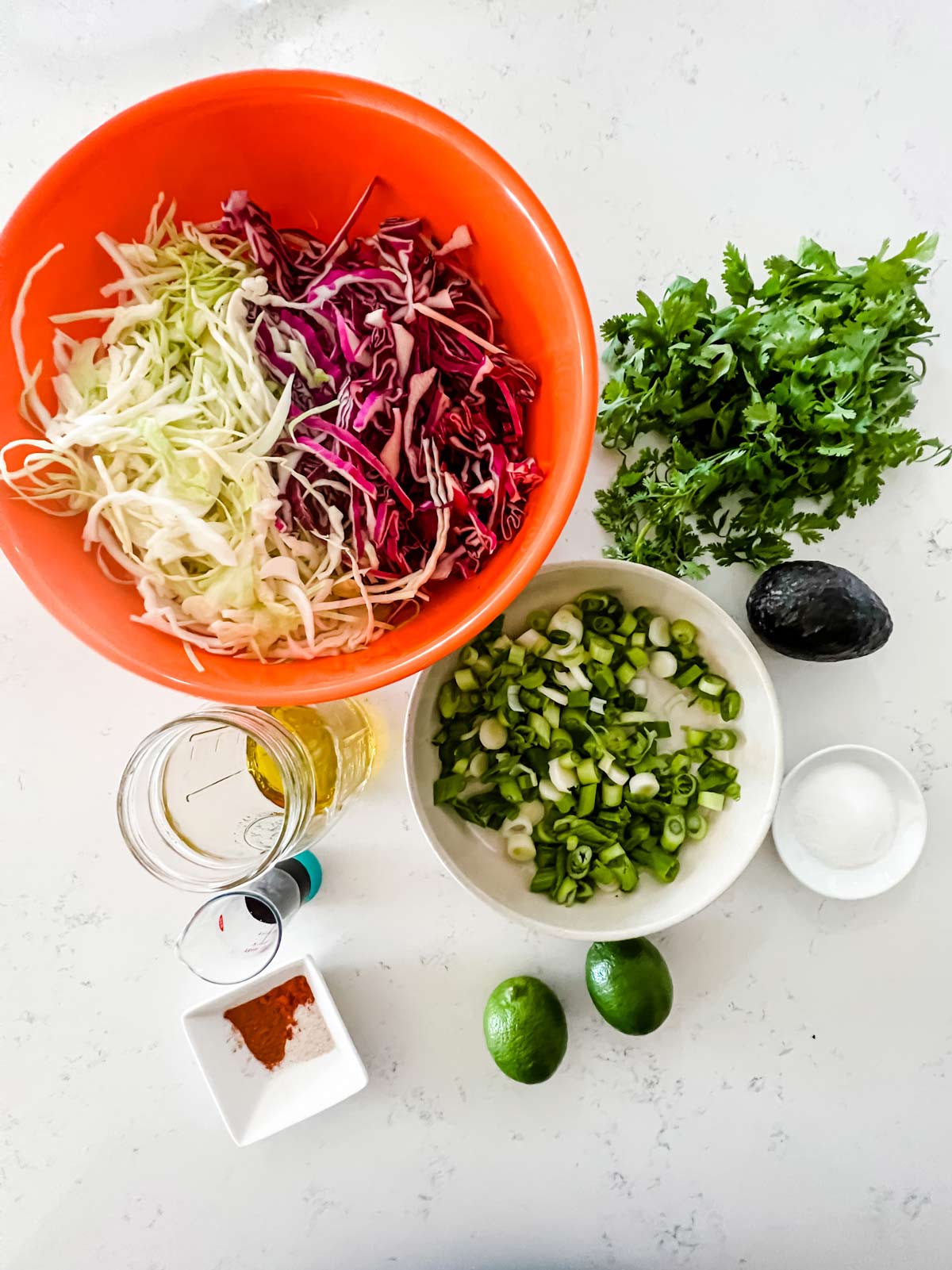 Overhead photo of shredded cabbage, cilantro, chopped green onions, avocado, sugar, lime, seasonings, oil, and soy sauce.