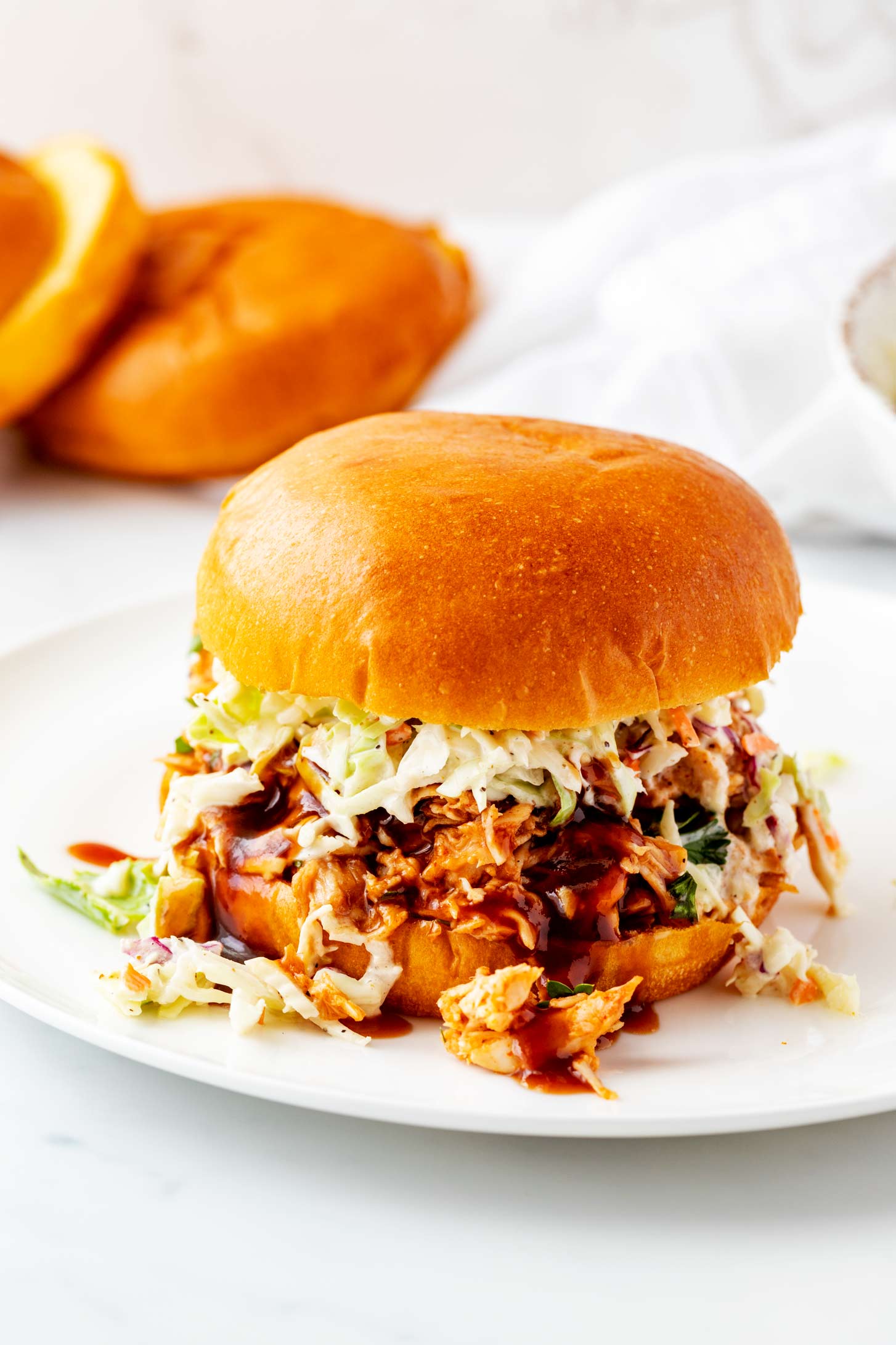 A BBQ Chicken sandwich with slaw on a white plate.