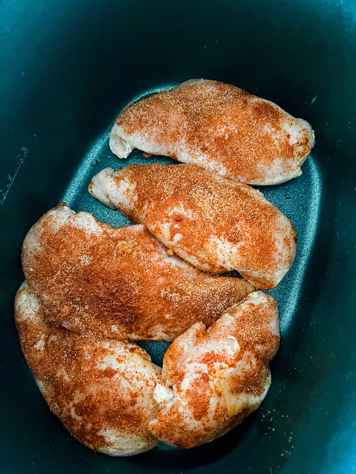 Seasoned chicken at the bottom of a slow cooker.