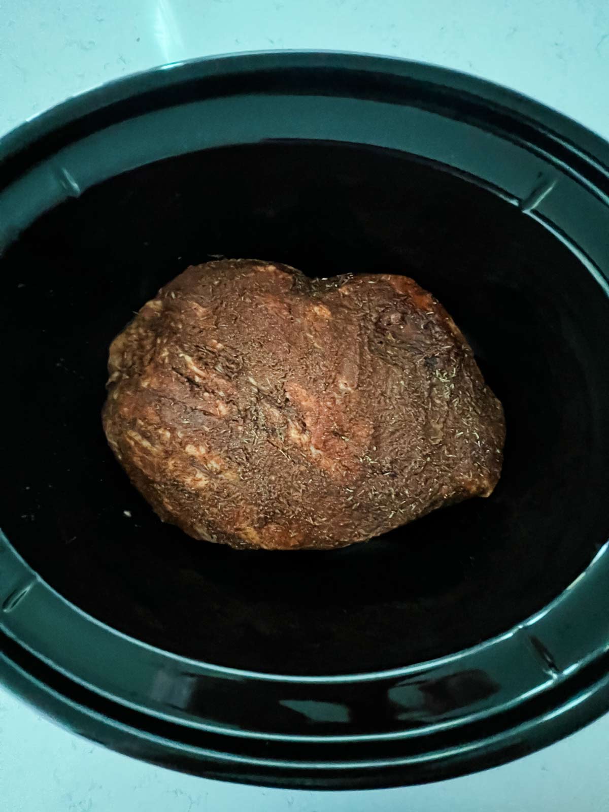 A seasoned brisket in the bottom of a slow cooker.