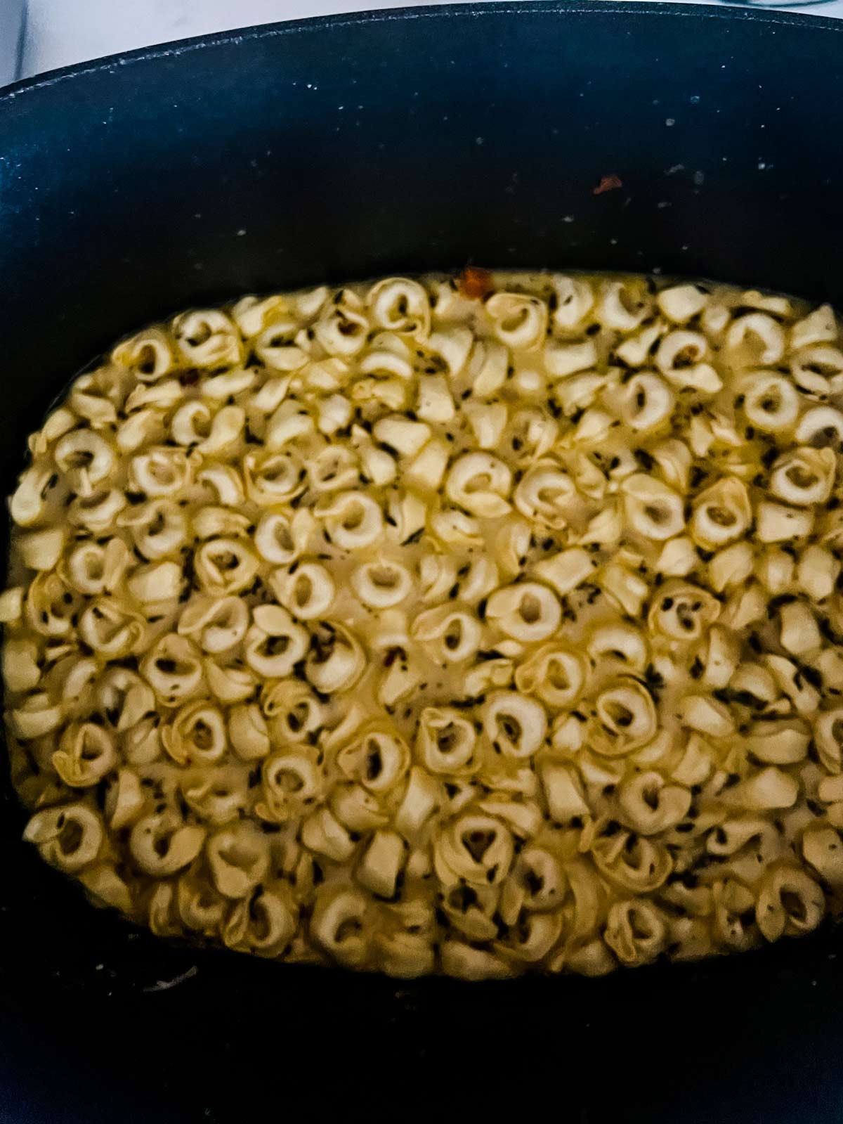 Dry tortellini being added to slow cooker tortellini soup.