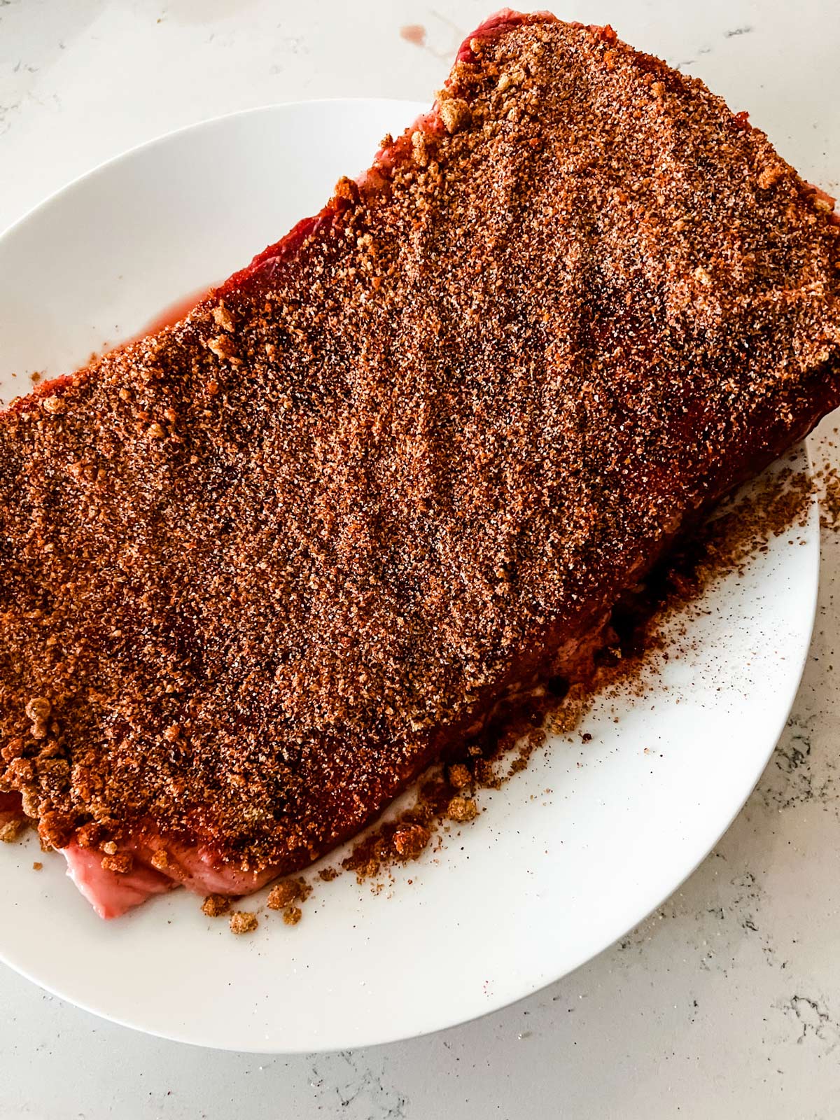 A brisket covered with dry rub on a white plate.