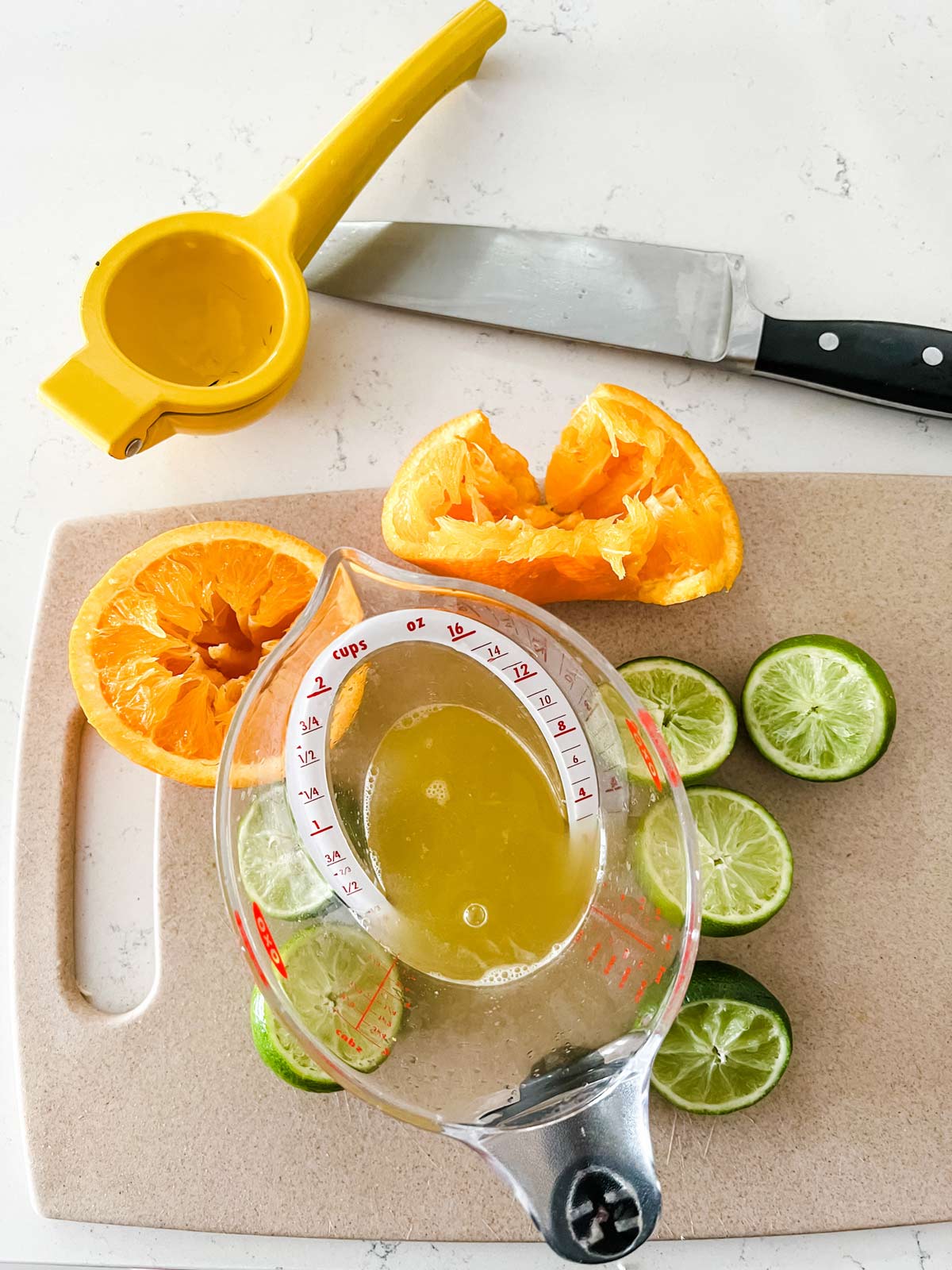 Citrus juices in a measuring cup with squeeze oranges and limes surrounding it.