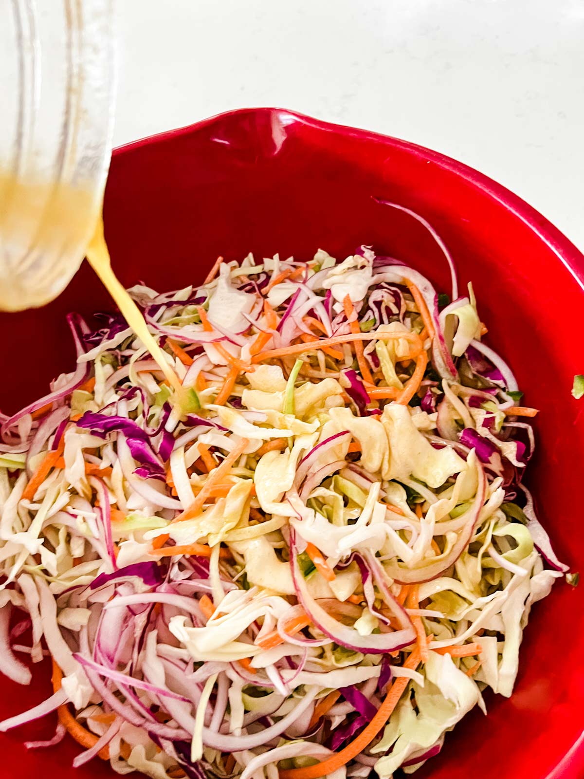 Slaw dressing being poured on top of Mexican slaw.
