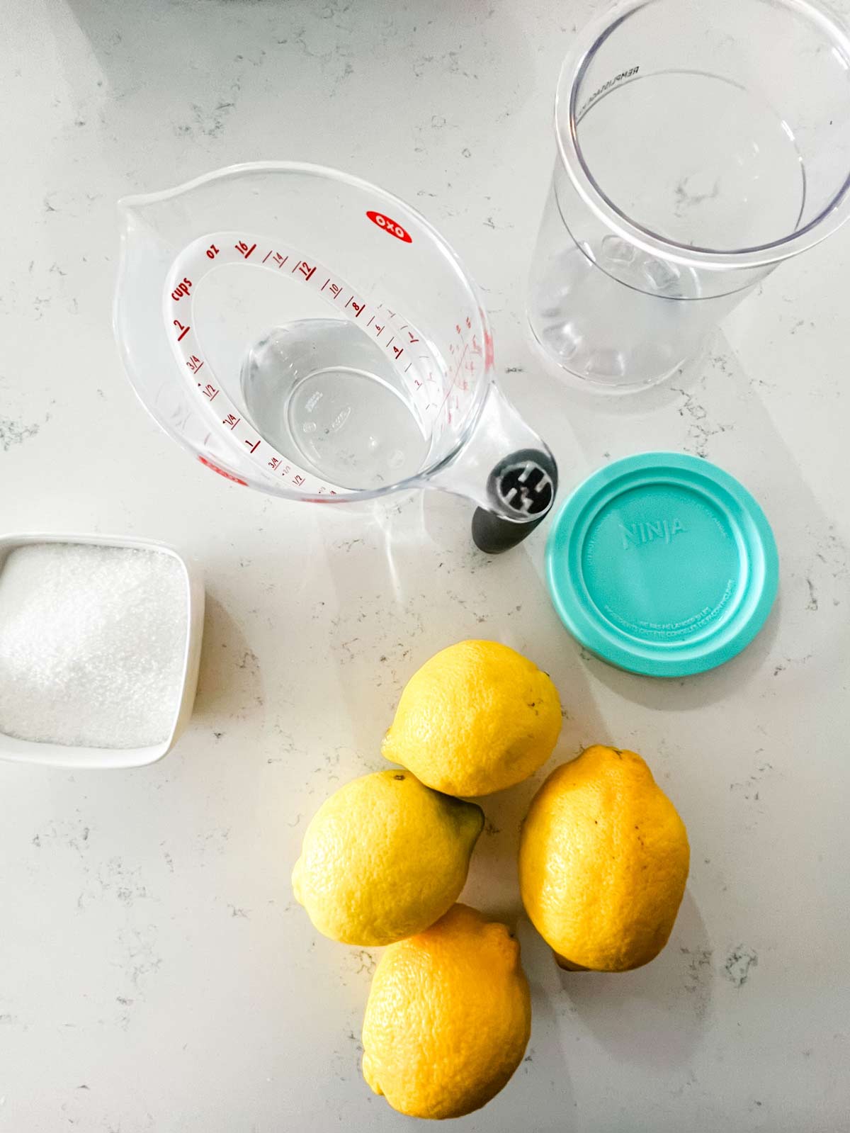Overhead photo of lemons, sugar, water, and a Ninja Creami pint.