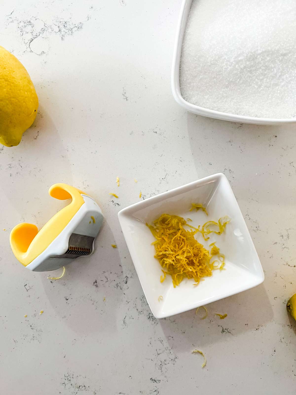 A small dish of lemon zest sitting next to a zester.