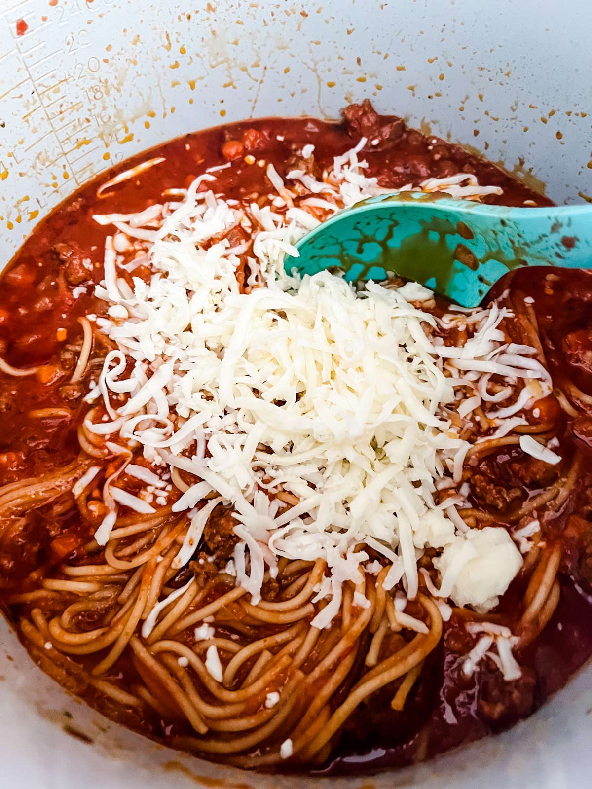 Cheese being stirred into cooked spaghetti in the inner pot of a Ninja Foodi.
