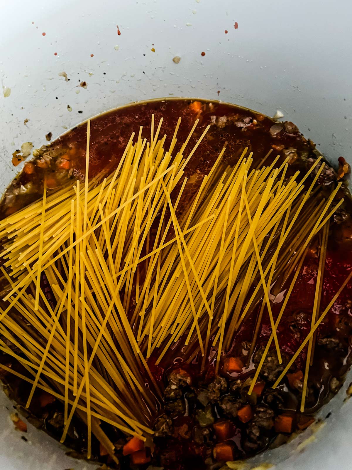 Raw spaghetti noodles on top of the meat sauce for in a Ninja Foodi inner pot.