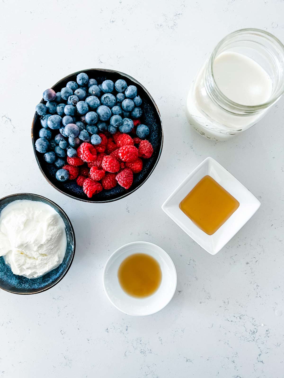 Ingredient shot photo with raspberries, blueberries, yogurt, milk, honey, and vanilla.
