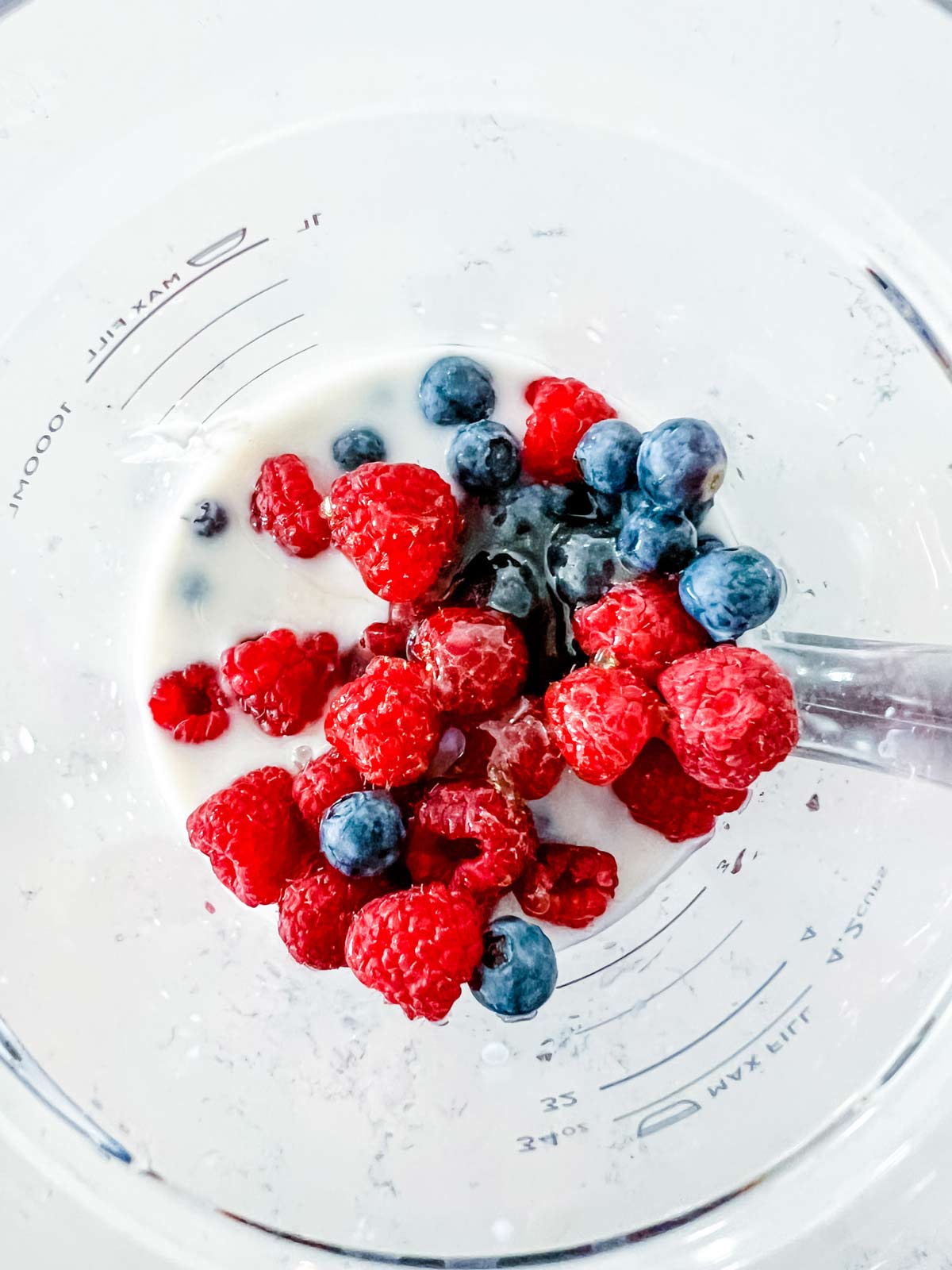 Milk, yogurt, vanilla, honey, raspberries and blueberries ready to be blended for a smoothie.