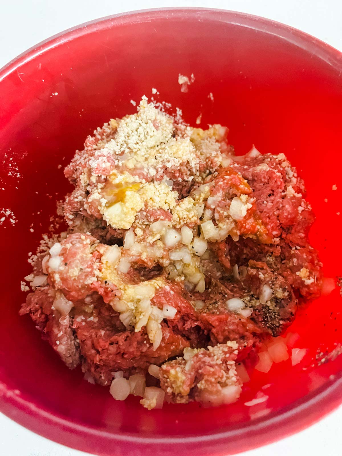 Ground beef being mixed with diced onion, egg, breadcrumbs and seasonings.