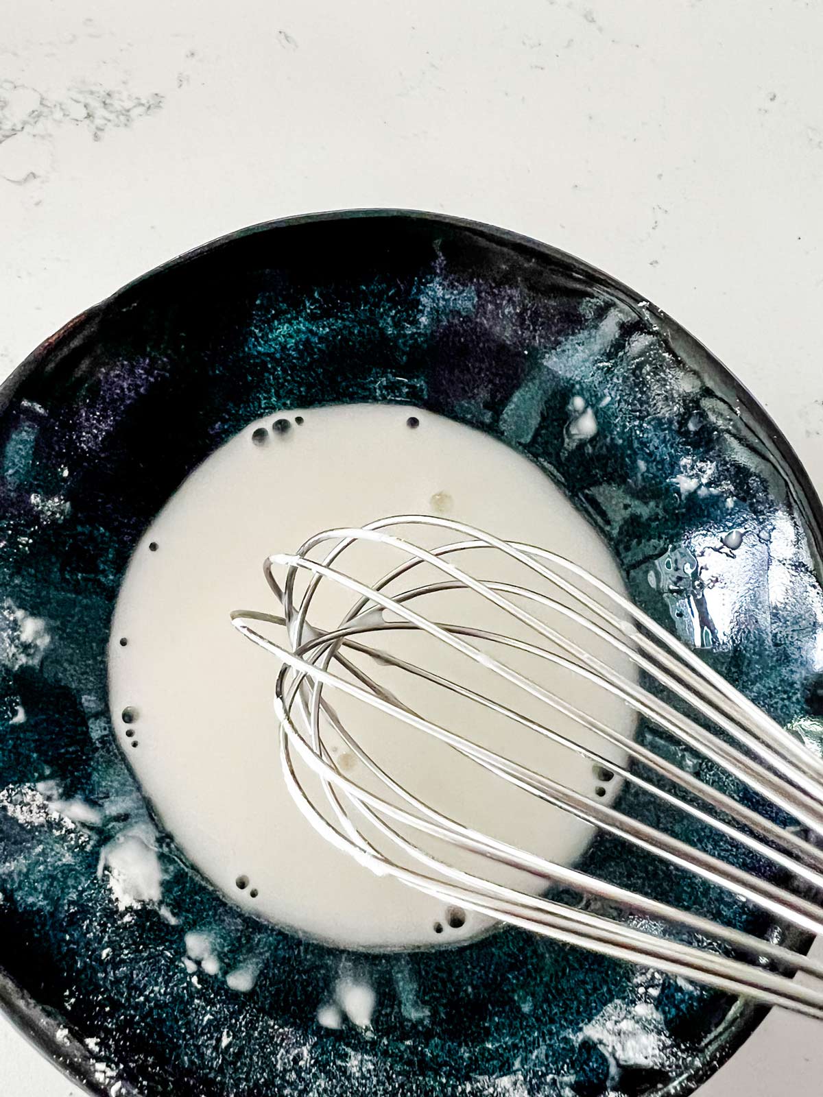 Water and cornstarch being whisked together in a small bowl.