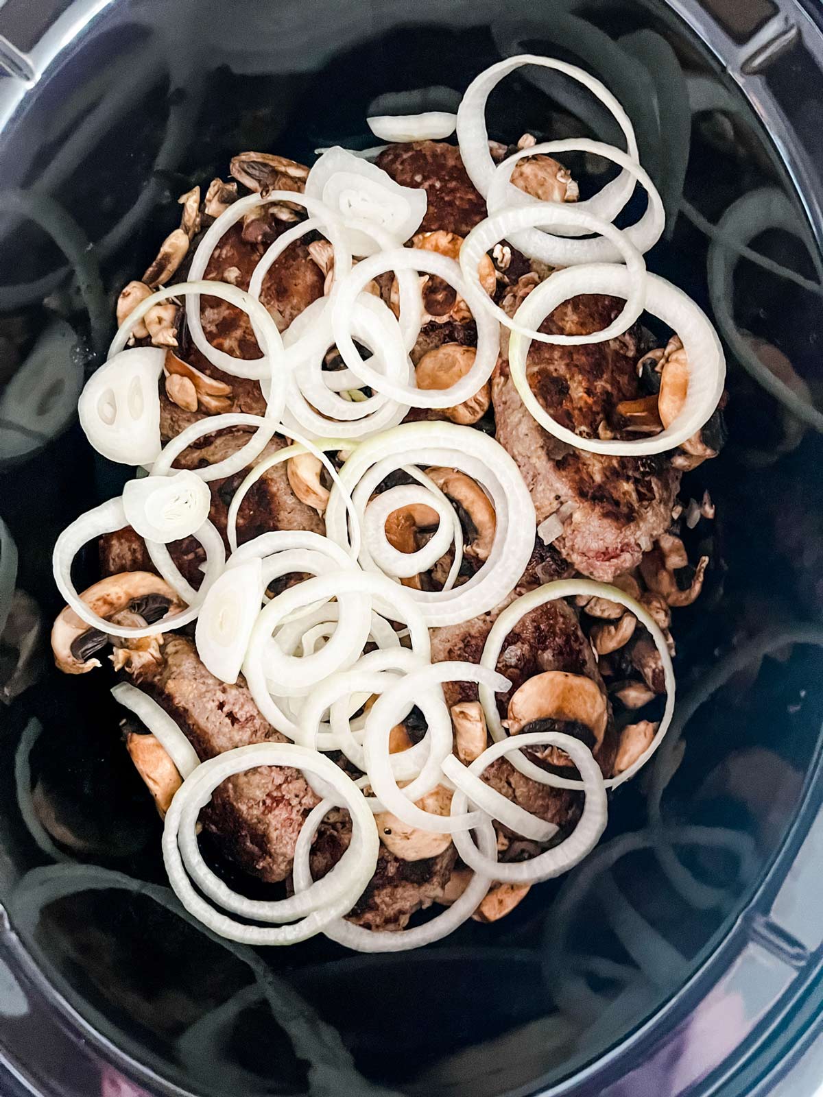 Onions and mushrooms over salisbury steak in a crockpot.