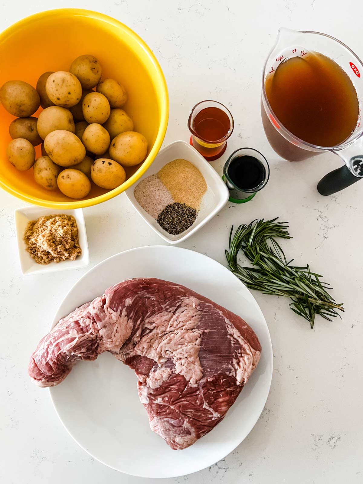 Overhead photo of a tr tip roast, baby potatoes, broth, rosemary, seasonings, 
avocado oil, broth, soy sauce, and brown sugar.