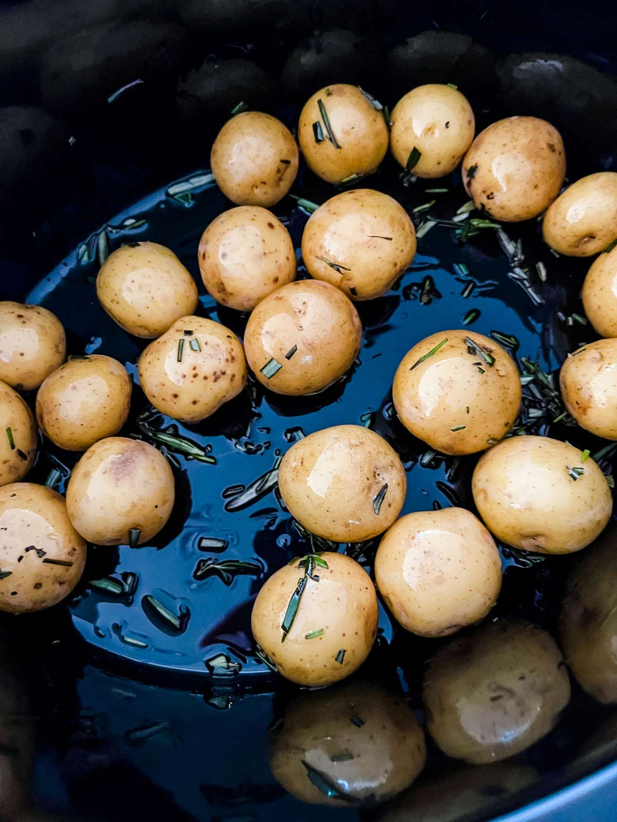 Overhead photo of baby potatoes tossed with rosemary and oil in the bottom of a slow cooker.