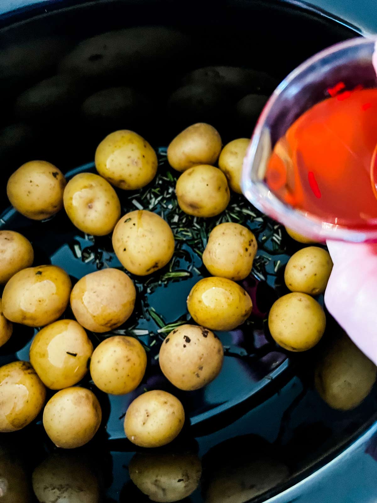 Oil being poured over baby potatoes in a slow cooker.