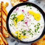 Overhead square photo of feta dip in a small blue bowl surrounded by dippers.