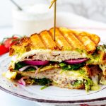 Square side photo of a turkey avocado panini on a rustic white plate.