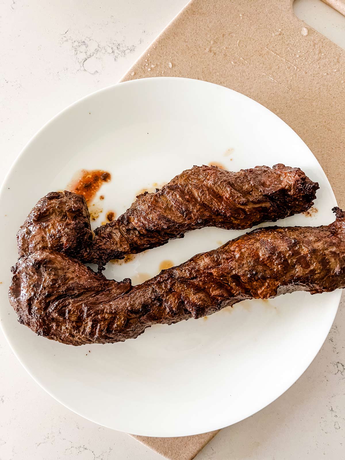Photo of grilled steak resting on a white plate.