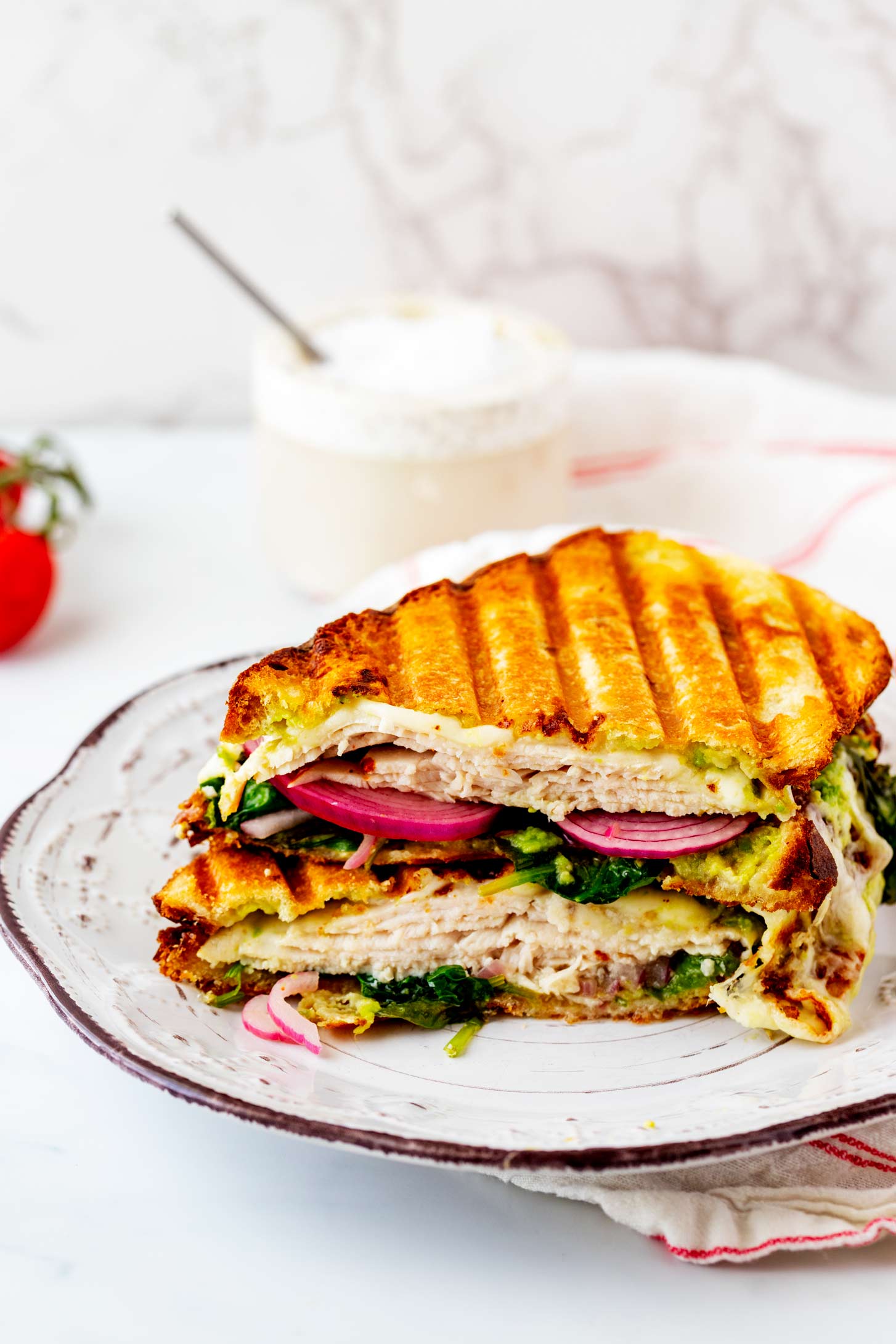 Photo of a rustic white plate with a turkey avocado panini on it.