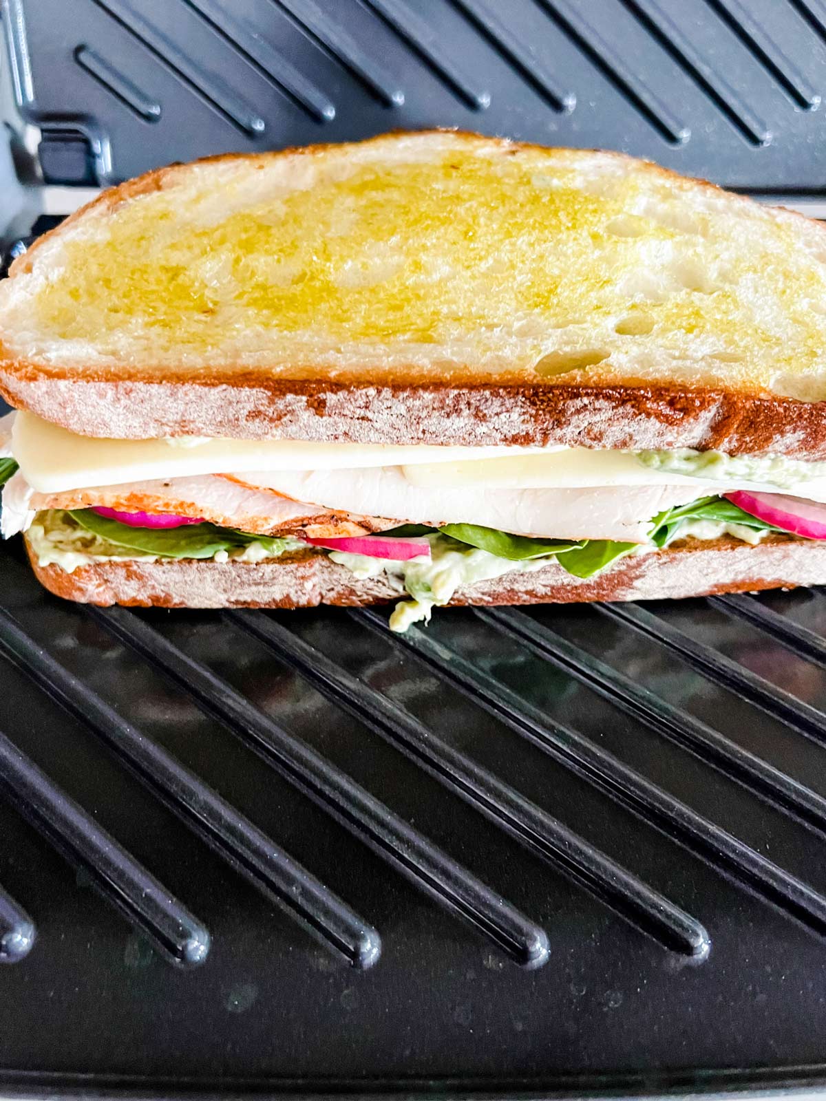 A turkey avocado panini that has just been added to a panini press.