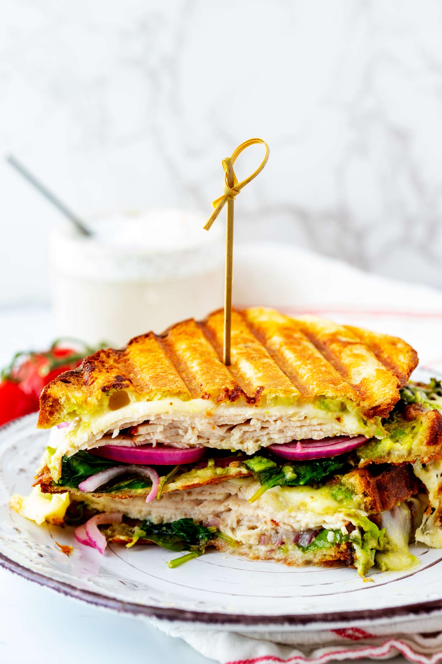 Side photo of a stacked turkey avocado panini with a skewer through it.