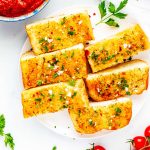 Square overhead photo of sliced air fryer garlic bread on a white plate with a small bowl of marinara next to it.